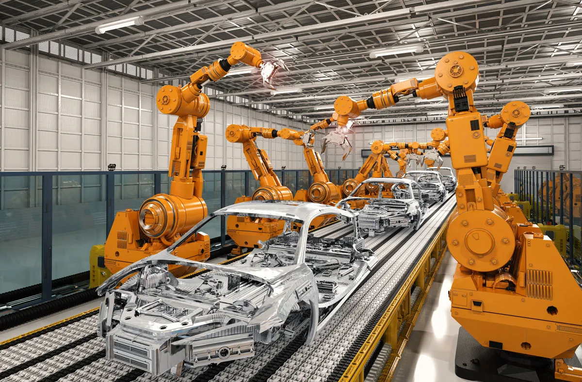 Orangefarbene Roboterarme montieren silberne Fahrzeugrahmen auf einer Fertigungsstraße in einem großen, gut beleuchteten Industriegebäude mit hoher Decke und Metallträgern.