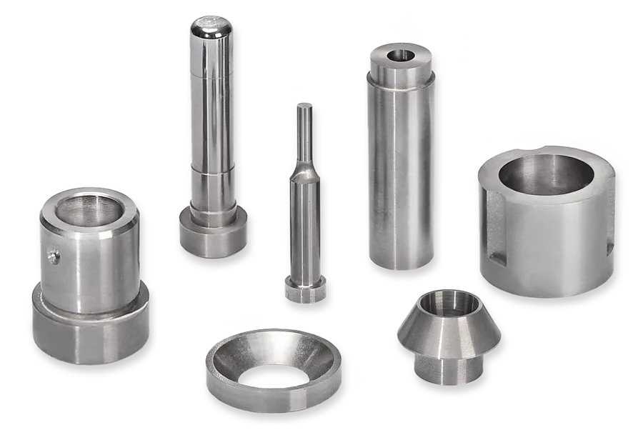 A set of precision-machined metal parts displayed upright and lying down, including cylindrical and ring-shaped components, all with a polished, metallic finish, on a white background with black stripes.
