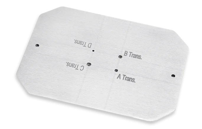 A rectangular metal plate with rounded corners, four small holes, and engraved labels reading A Trans., B Trans., C Trans., and D Trans. positioned in separate quadrants.