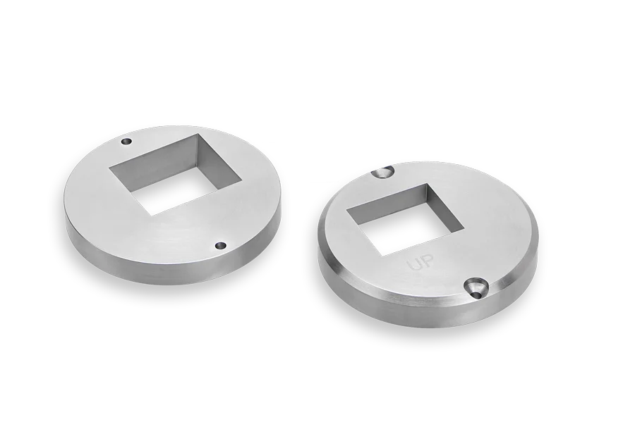 Two round, silver metal plates with square cutouts in the center are shown against a black background. One plate has UP engraved on it; both plates have small holes near the edges.